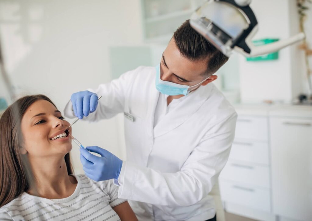 Dentist performing a routine dental exam on a smiling patient during a preventive checkup to monitor long-term oral health.